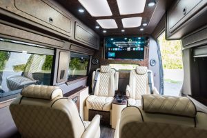 Interior of a luxury van rental in Tennessee featuring leather captain’s chairs, smart TV, and wood paneling—ideal for executive transport or chauffeur services by Woosh.