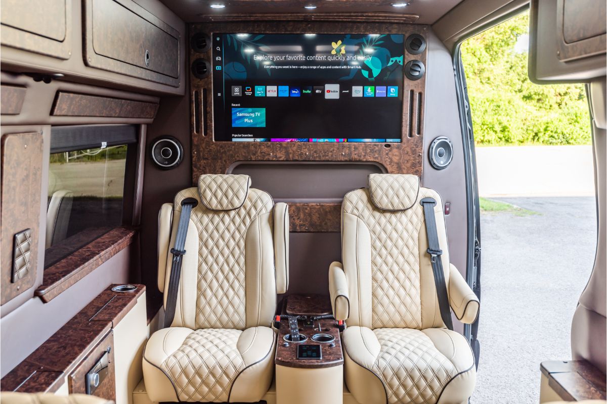 Interior of a luxury van rental featuring leather captain’s chairs, smart TV, and premium finishes.