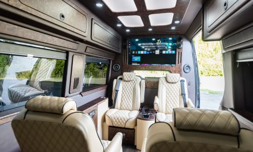 Interior of a luxury van rental in Tennessee featuring leather captain’s chairs, smart TV, and wood paneling—ideal for executive transport or chauffeur services by Woosh.