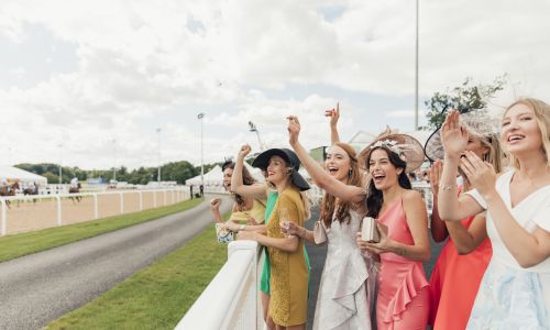 A group of young women cheering on the horses as they race by on the track 